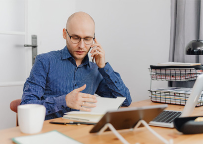 bald, bespectacled man in blue shirt reading and talking on phone